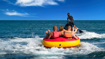 Water tubing. A group of tourists in life jackets rides on an inflatable ring towed by a jet ski. An extreme boat ride. © ROMAN DZIUBALO