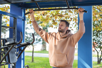 Man training outdoors on pull-up bar, focusing on strength and fitness during morning workout in a park environment with sunlight and greenery, showing healthy lifestyle and active routine