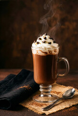 tall glass mug of hot chocolate topped with whipped cream and mini chocolate chips.