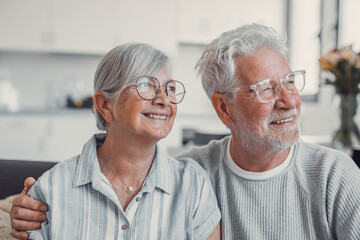 Happy senior couple relaxing together at home on sofa, elderly retired woman and partner looking out the window while sharing a calm moment, enjoying peaceful domestic life and emotional connection