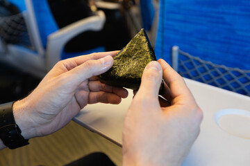 A man opening the wrapper of an onigiri, a rice ball wrapped in seaweed and filled with tuna and...