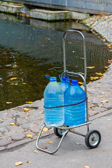 Plastic bottles of water on a metal wheelbarrow, standing on an asphalt road near a river or pond