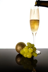 Serving champagne on classic glass next to Christmas ball and bunch of grapes