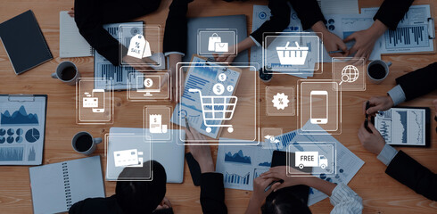 A diverse group of professionals collaborates in a marketing strategy meeting. Digital icons representing e-commerce and business insights overlay their detailed discussion materials. Trope