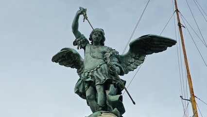 Rome, Italy - 12 January 2025. The bronze statue of Archangel Michael atop Castel Sant&rsquo;Angelo is shown with raised sword and outstretched wings under a grey sky.