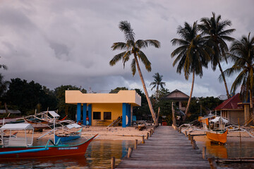 Scenic Coastal View with Boats, Wooden Pier, Palm Trees, and Tropical Clouds