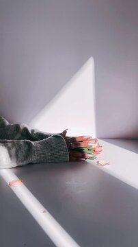 a hand gently holding blush pink roses and greenery on a white surface, illuminated by natural light with soft shadows and scattered petals.