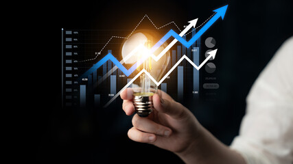 A hand holds a glowing light bulb symbolizing innovative ideas and growth, paired with dynamic graphs and data showcasing financial success and progress. Scalp