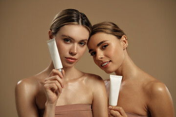 Beautiful women holding cosmetic skincare tubes on beige background