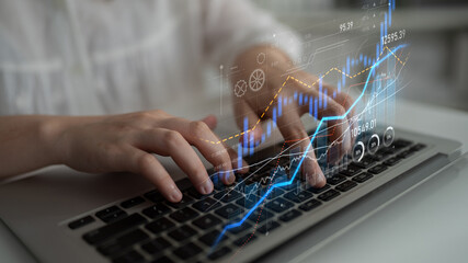 A close-up of hands typing on a laptop keyboard with a digital overlay of financial graphs. This image represents the intersection of technology and finance in today business environment. Scalp