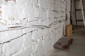 A white brick wall shows exposed electrical wiring and a wooden block on the concrete floor in a workspace