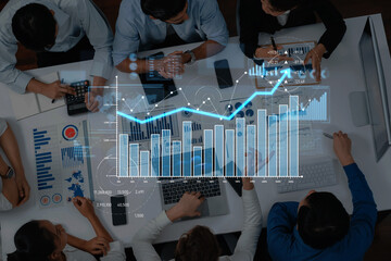 A group of business professionals engage in financial analysis, utilizing laptops and tablets to visualize data trends and discuss strategies in a collaborative office setting. Scalp