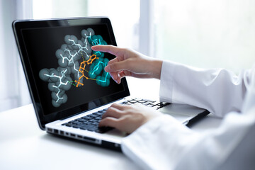 Closeup of researcher hand pointing at a laptop screen displaying 3D molecular model. Computational simulation shows protein drug interaction. Concept of biotechnology, medicine research.