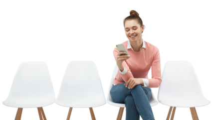 Happy young woman sitting on chair laughing while reading funny message or content on smartphone