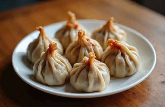 Steamed Mongolian buuz dumplings filled with juicy minced beef rest on white plate. Parcels of handmade dough served warm on rustic wooden table, offering savory taste of traditional cuisine.