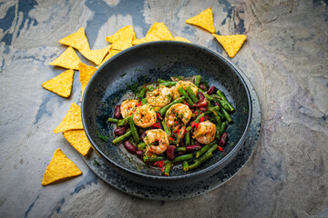 Traditional Mexican style kidney beans and green beans strew salad with prawns, lime and  tortilla chips served as close-up on a design plate