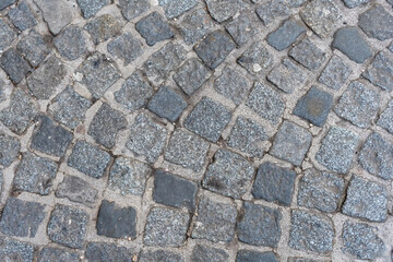 Gray stone pavement made of uneven granite cubes as the urban backdrop of an ancient European street