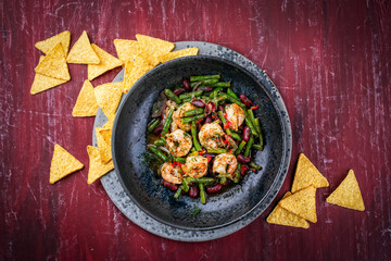 Mexican style kidney beans and green beans strew salad with prawns, lime and  tortilla chips served as top view in a design bowl