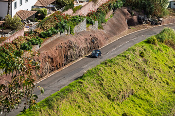 View from above of a mountain road with a small car driving along it. Country road in volcanic rocks