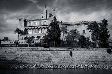 Historic fortress and palace beside the waterfront under a blue sky. Mediterranean landmark with stone walls, palm trees and reflections.