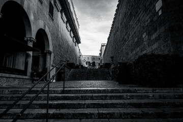 Narrow Mediterranean old town street with stone buildings, plants and cobblestone pavement.