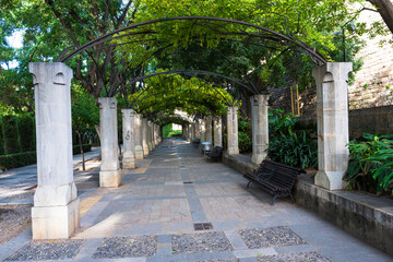 Symmetrical garden fountain surrounded by trees and greenery in a historic park. Peaceful Mediterranean outdoor space with water and shade.