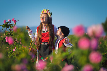 Bulgarian rose valley near Kazanlak, Bulgaria young girl and boy siblings in ethnic folklore clothes harvesting blooming oil-bearing roses at sunrise