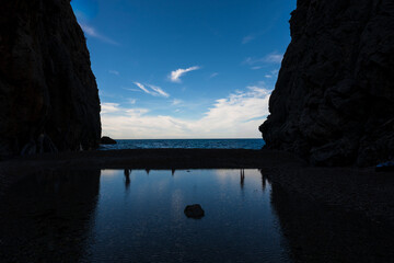 Mediterranean coastal landscape with calm sea, natural reflections and rocky cliffs framing the blue horizon.