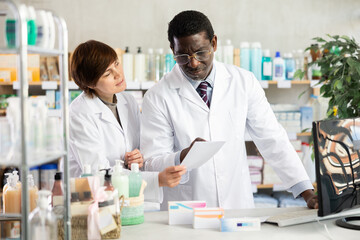 Fototapeta premium Adult male and adult female pharmacists checking medical prescription on computer in pharmacy