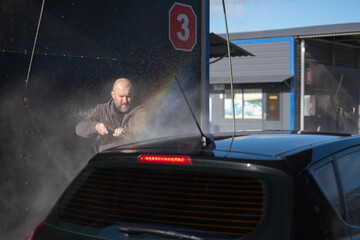 Man washing a car at a car wash location during daytime