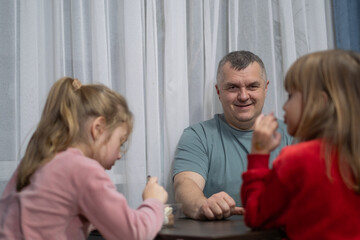 Smiling man enjoys dessert with two young girls in a cozy indoor setting during the evening