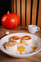 Cheese pancakes with fruit sauce served for breakfast, coffee cup and pumpkin in soft focus background. Warm autumn light, cozy mood and rustic lifestyle food composition.