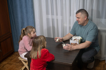 Man shares dessert with children at home during evening gathering around a small table near a window