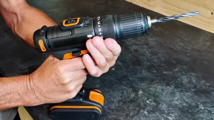 DIY expert using a cordless power drill to make a hole in a wooden surface. Craftsman's hands holding the electric tool during a home improvement project in his workshop or garage