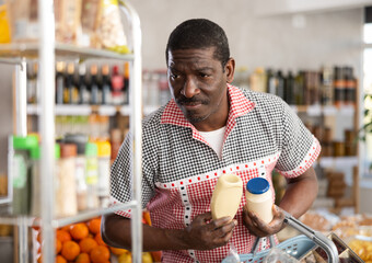 Adult man buyer choosing mayonnaise sauce in bottle or jar in grocery store
