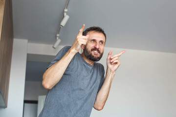 Smiling adult man indoors raising hands in playful gesture, casual home lifestyle moment, positive...