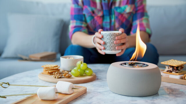 Portable tabletop fire pit with bioethanol flame on marble table, cozy indoor setup with snacks and hot drink, mini fire burner for home, small fireplace for balcony or living room ambiance