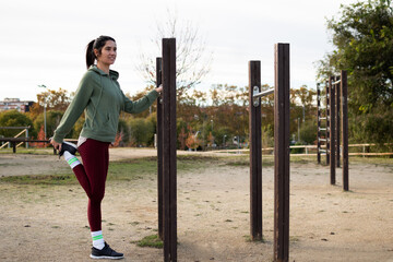 Woman performing a quad stretch on calisthenics equipment in an outdoor park