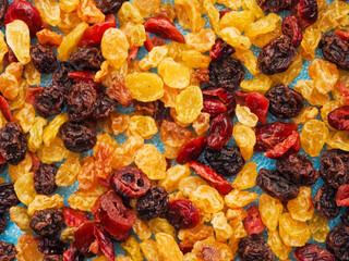 A close up of dried fruit with a blue background. The fruit is a mix of raisins, cranberries, and other dried fruits. The colors of the fruit are bright and vibrant, creating a cheerful mood