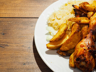 Chicken drumsticks and spicy potato wedges meal with sauerkraut salad on a plate. Simple tasty cooked meal.
