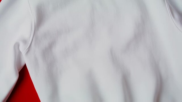 A close-up of a white sweatshirt on a red background, showcasing the fabric texture and contours