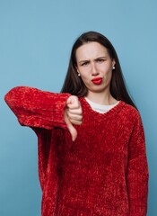 Young woman shows dislike with thumbs down gesture against blue background