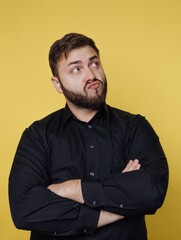 Fototapeta premium Man with beard looks up while crossing arms against yellow background in indoor setting