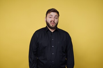 Obraz premium Man with beard stands in front of yellow background, making a funny face during a casual moment in a studio setting