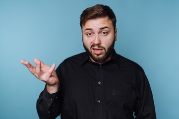 Fototapeta premium Man in black shirt gestures with hand while explaining something in front of a blue background