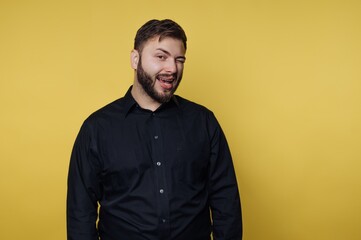 Obraz premium Man smiles and winks while standing against a yellow background in a studio setting during the daytime