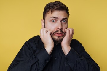 Man shows surprise in front of yellow background while holding his face with both hands in a moment of shock or disbelief