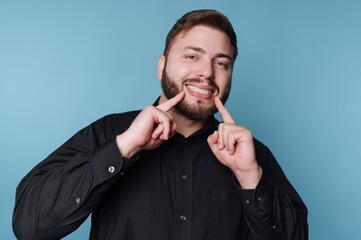 Smiling man showing teeth with hands against a plain blue background during a casual moment