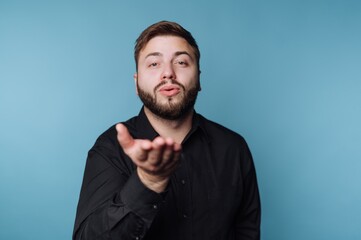 Obraz premium Young man blowing a kiss while wearing a black shirt against a blue background in a studio setting
