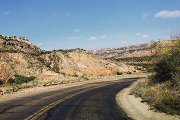 Curving desert road through rocky hills. Empty asphalt highway in arid landscape. Scenic route under blue sky. Travel adventure in remote American wilderness. Perspective view of transportation.